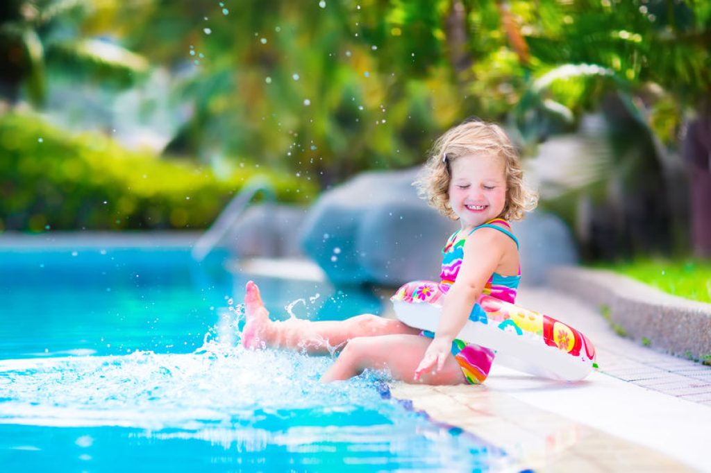 Cette fillette s'amuse a taper des pieds dans l'eau d'une piscine.
