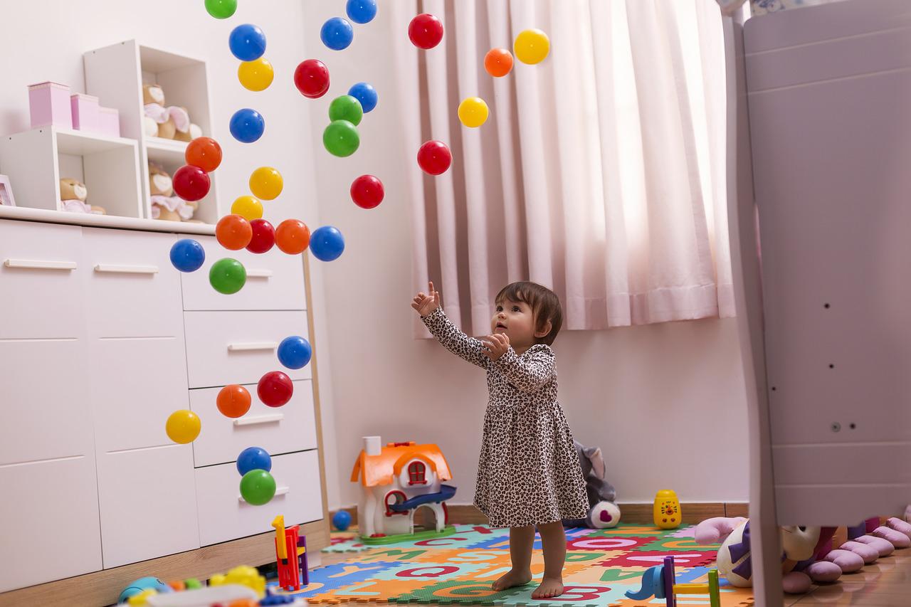 Cette petite fille est en train de jouer et d'admirer les balles en plastique jetées en l'air.