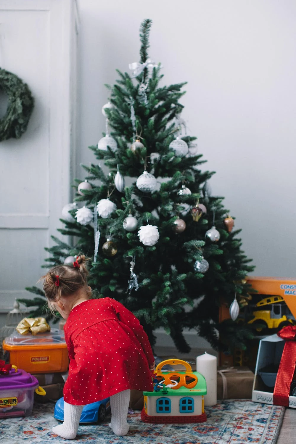 Ce bébé regarde des jouets au pieds du sapin.