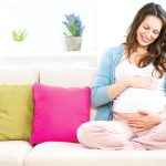 Cette future maman est assise sur un canapé.